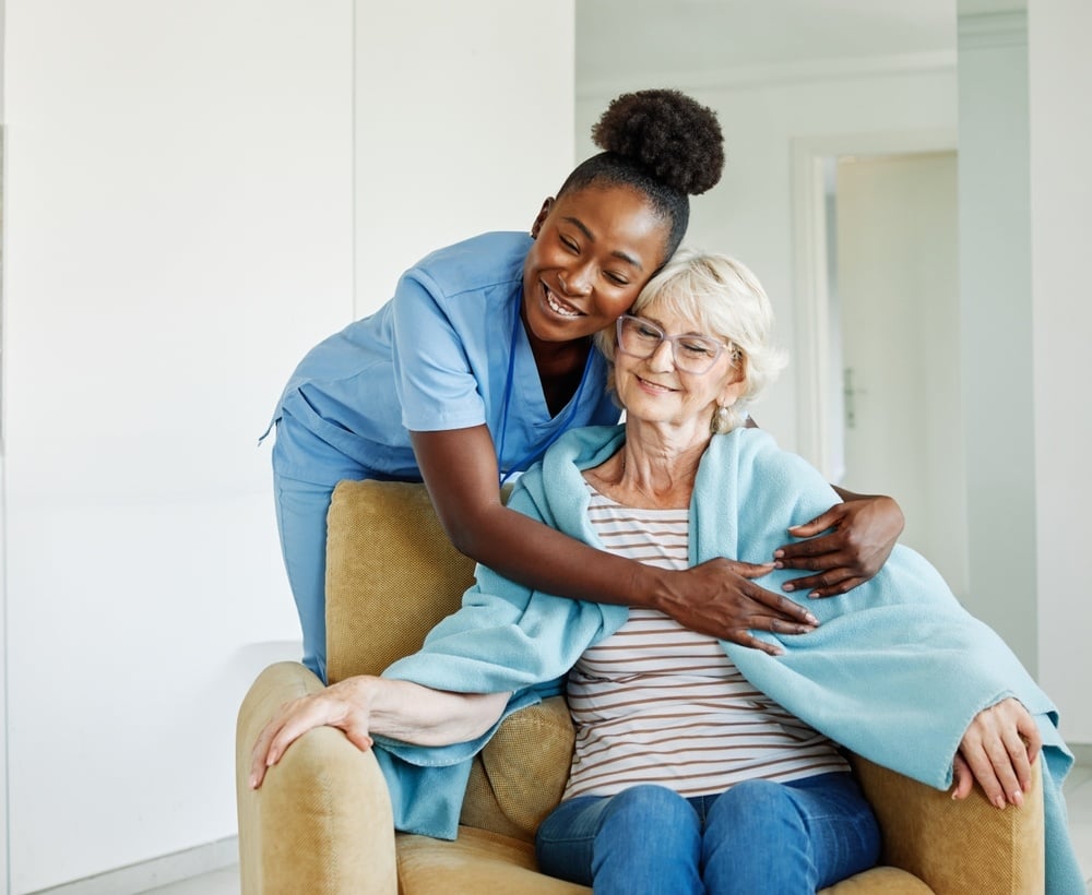 Home Health Aide smiling and hugging patient in her home